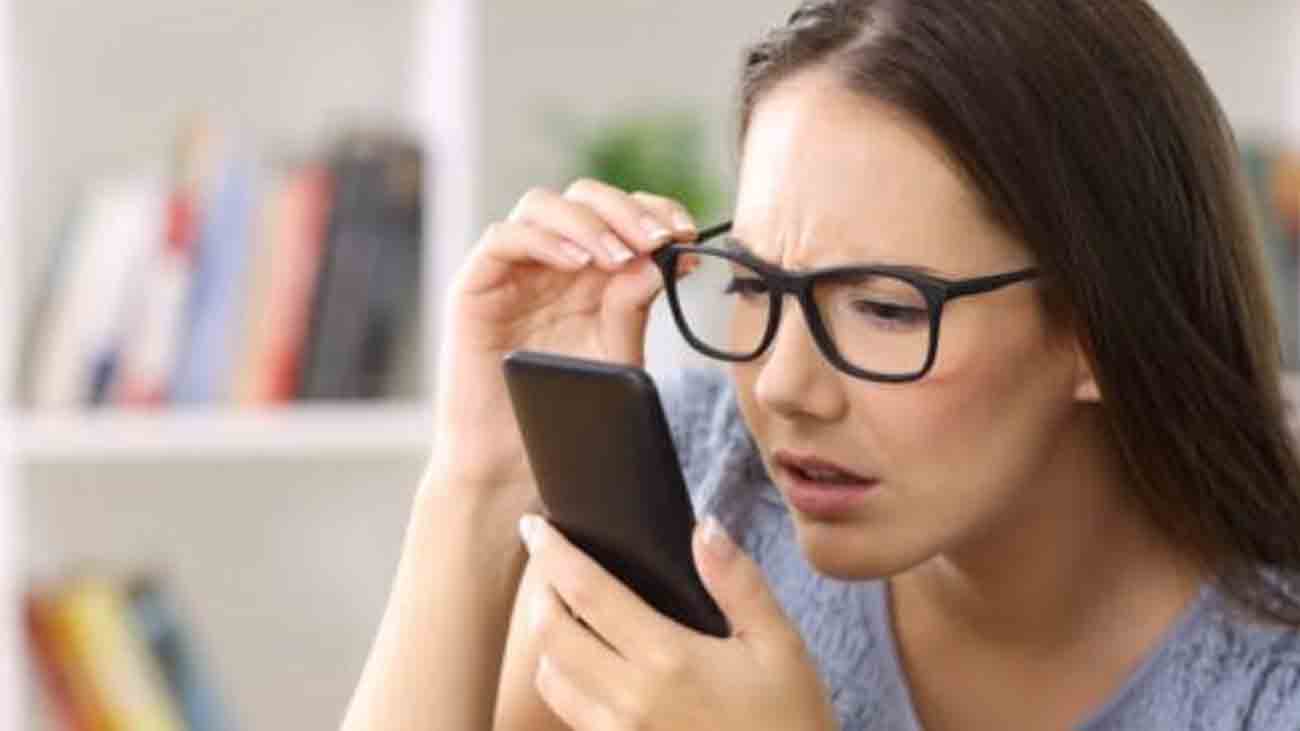 A woman is trying to read something on a mobile phone with glasses on her eyes.