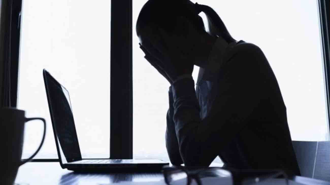 A woman who is a victim of online sexual exploitation sits in front of her laptop with her hand over her mouth.