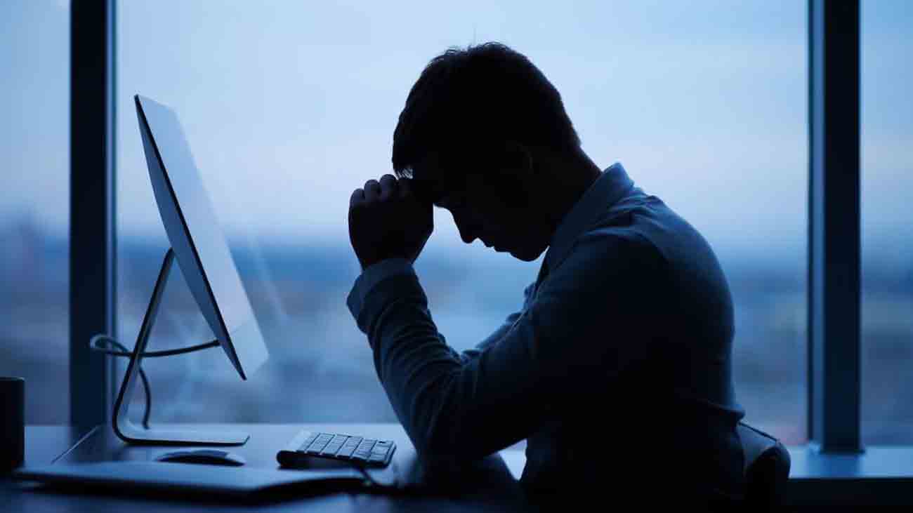 A depressed man sits in his office with his head down.