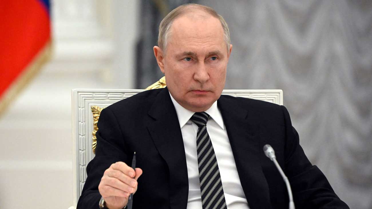 روسی صدر کالا کوٹ پینٹ اور ٹائی پہنے بیٹھے ہیں، ان کے ہاتھ میں پین ہے