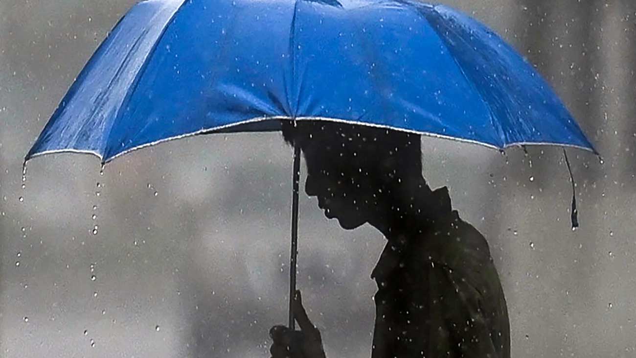 ایک شخص بارش میں چھتری لے کر جا رہا ہے