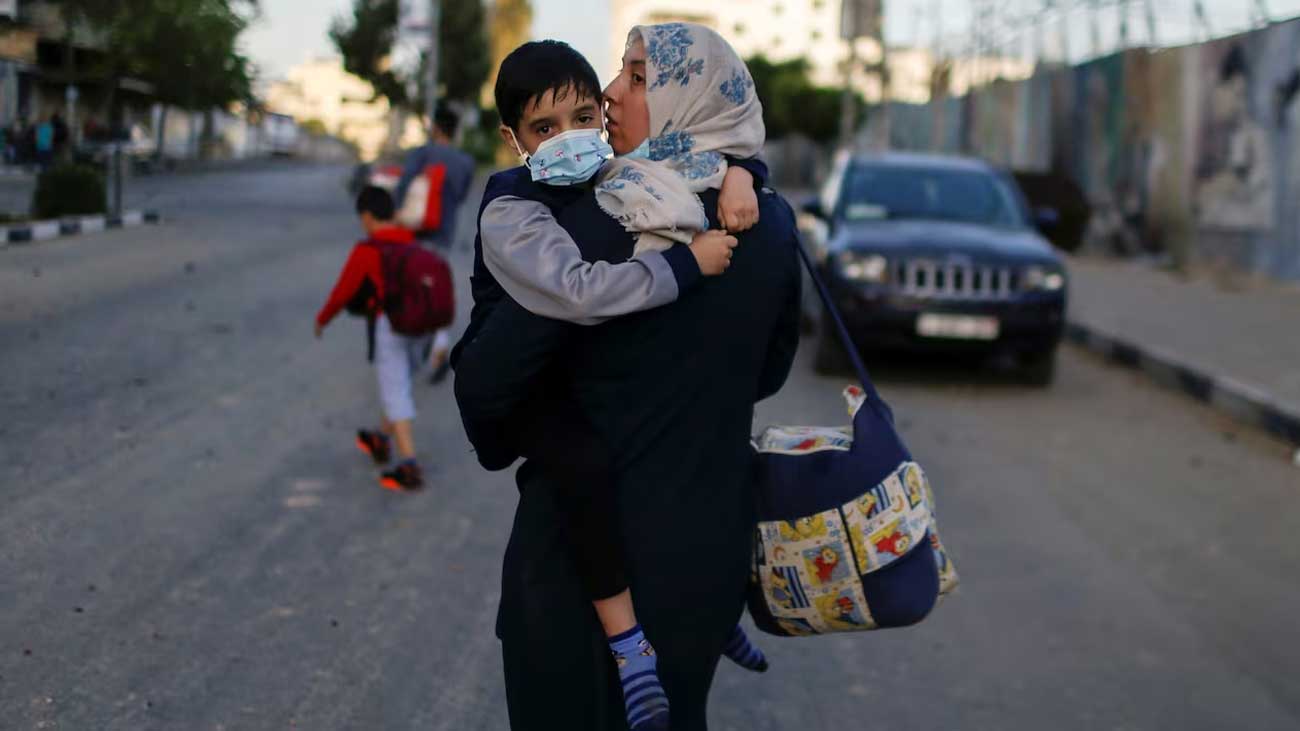 ایک فلسطینی خاتون غزہ کے جنگ زدہ علاقے سے اپنے بچے کو گود میں اٹھائے جا رہی ہے
