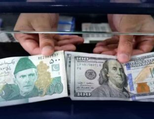 ایک شخص اپنے ہاتھوں میں ڈالر اور پانچ سو روپے کا نوٹ پکڑے کھڑا ہے