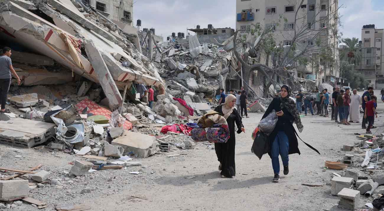Palestinian women walk by buildings destroyed in Israeli airstrikes
